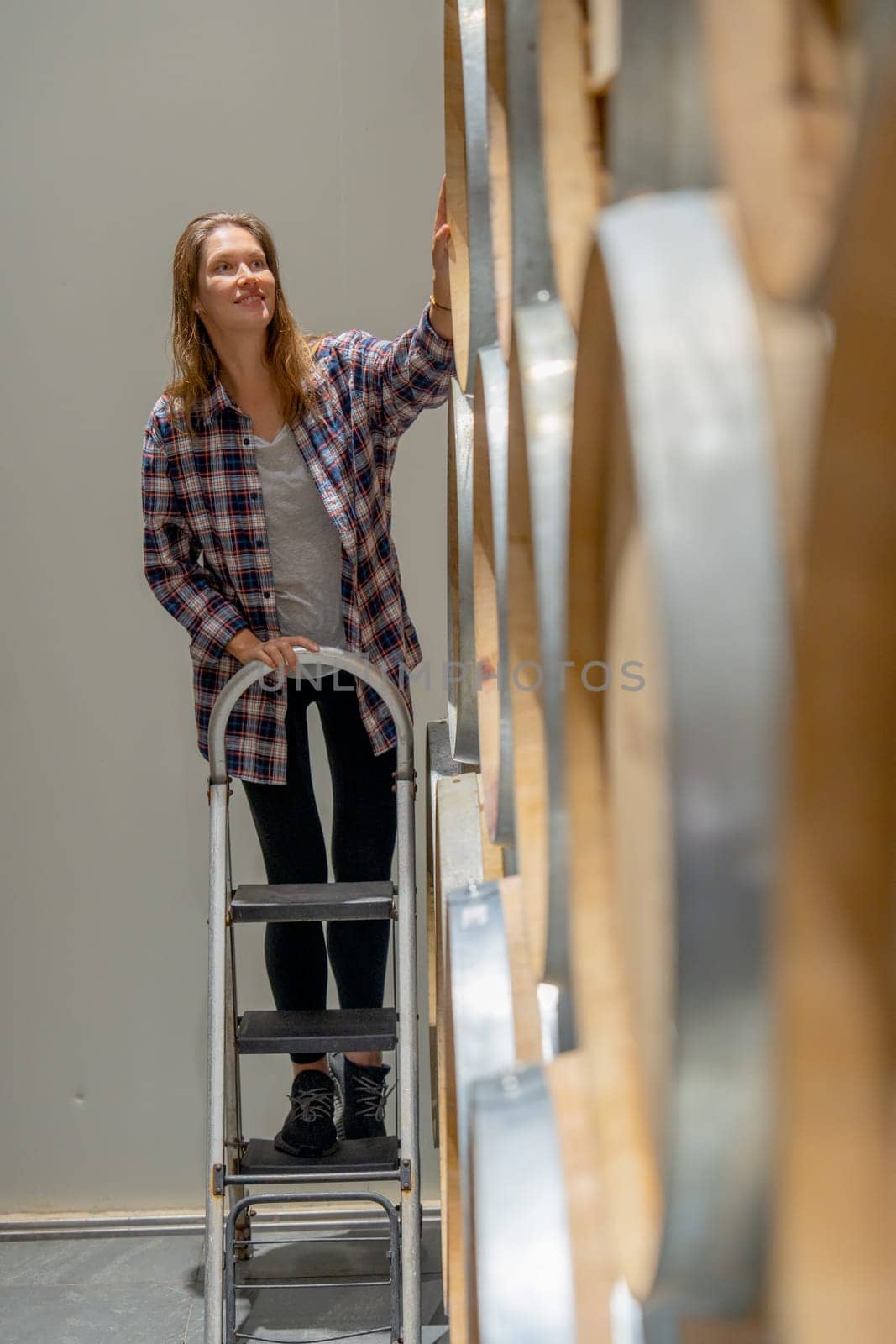 Vertical image of winery worker woman stand on the stairs to check the product in modern factory.