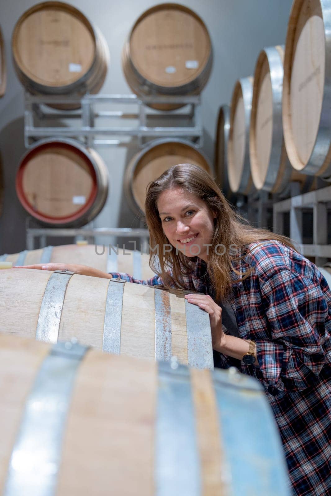 Vertical image of winery worker woman stand near wine fermentation tank and check the product in modern factory and she also look at camera with smiling.