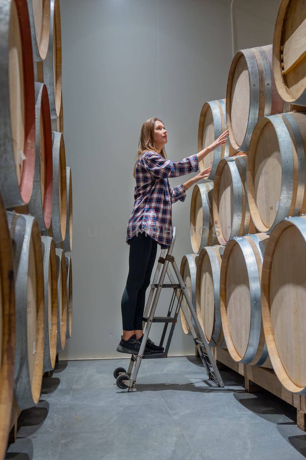 Vertical image of winery worker woman stand on the stairs to check the product in modern factory.