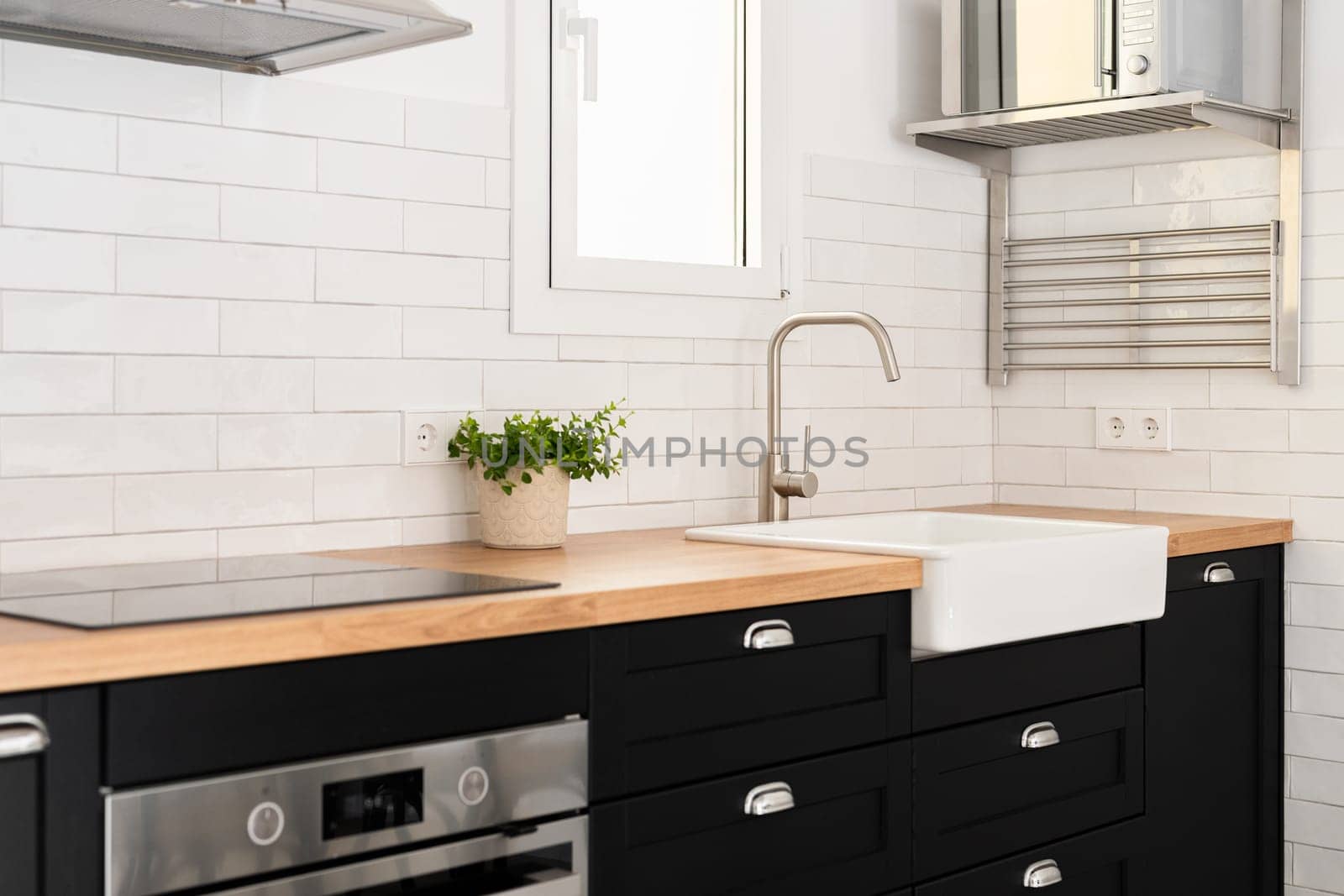Washing sink with faucet by window in modern kitchen. Appliances and furniture in cooking zone of modern apartment. House interior