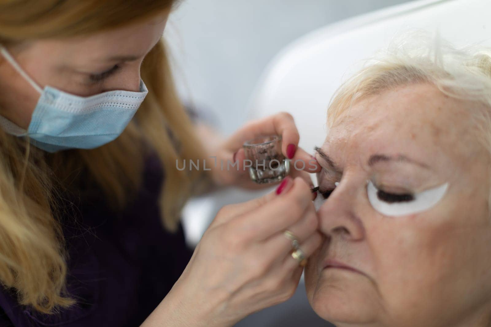 A woman using the services of a beautician has special cotton pads taped under her eyes. Thanks to them, henna tinting eyelashes will not stain the skin around the eyes.