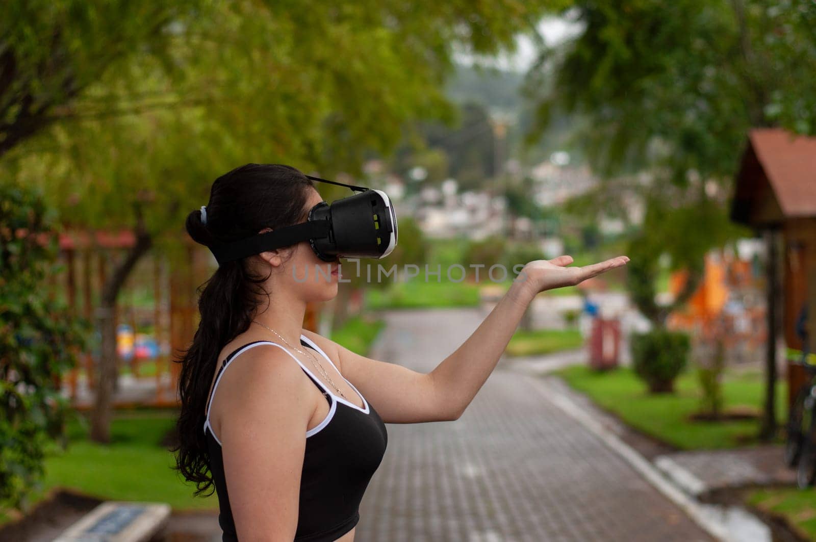 copyspace of a girl wearing virtual reality goggles and sportswear with her hand in the air in a public park. by Raulmartin