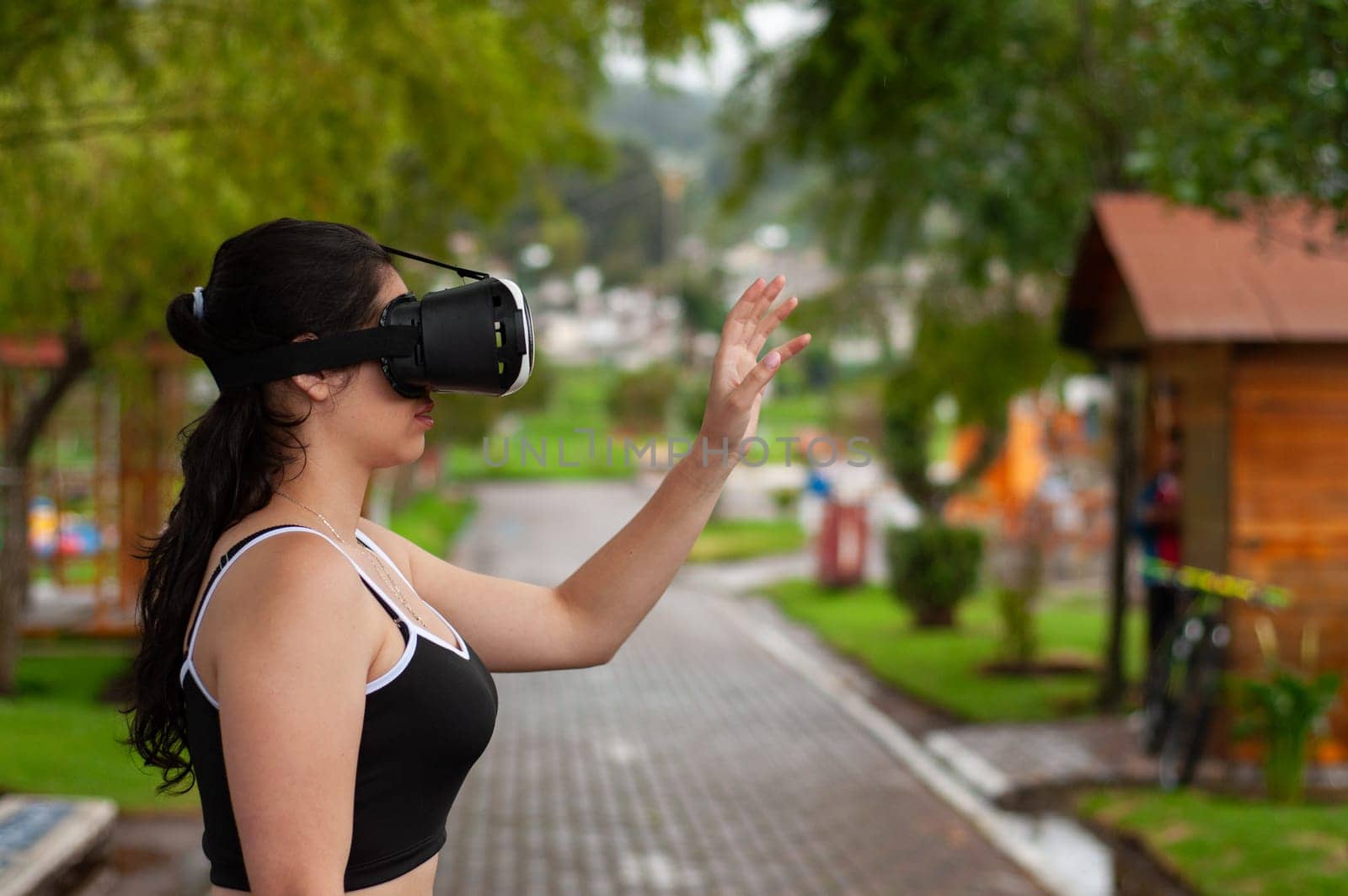young girl in a park wearing augmented reality glasses with her hand raised touching a reality that does not exist. by Raulmartin
