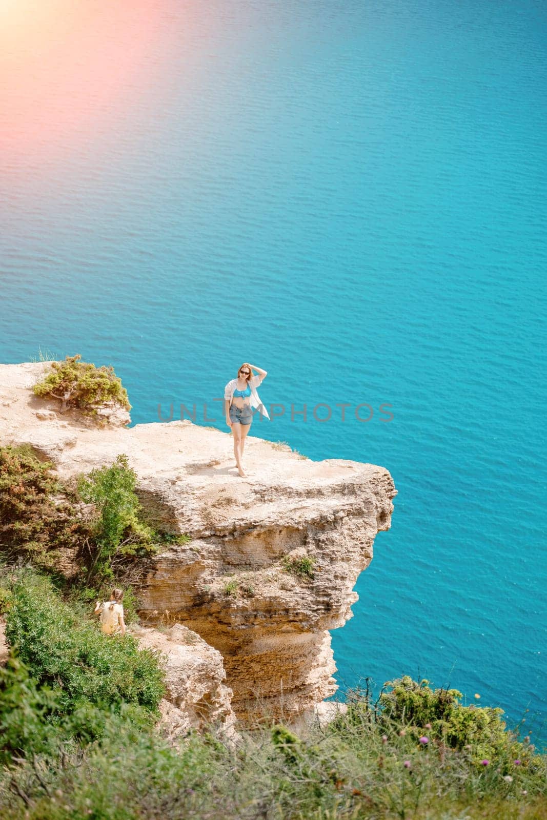 Woman travel summer sea. Portrait of a happy woman on a background of rocks and the sea. View of a woman in a white shirt and swimsuit. Freedom and happiness.