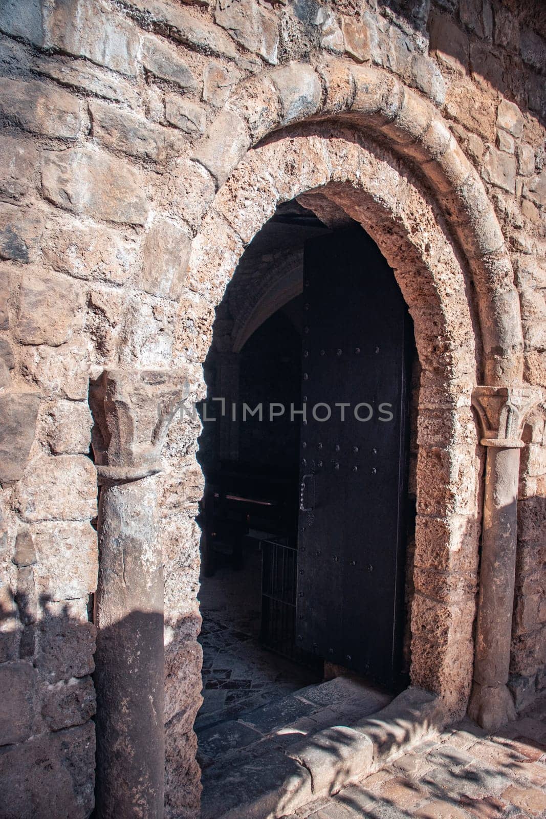 Black door leading in ancient church photo. Beige brick textured wall photography. Entrance with two shutters. Sant Miquel del Fai monastery photo. High quality picture for wallpaper, article