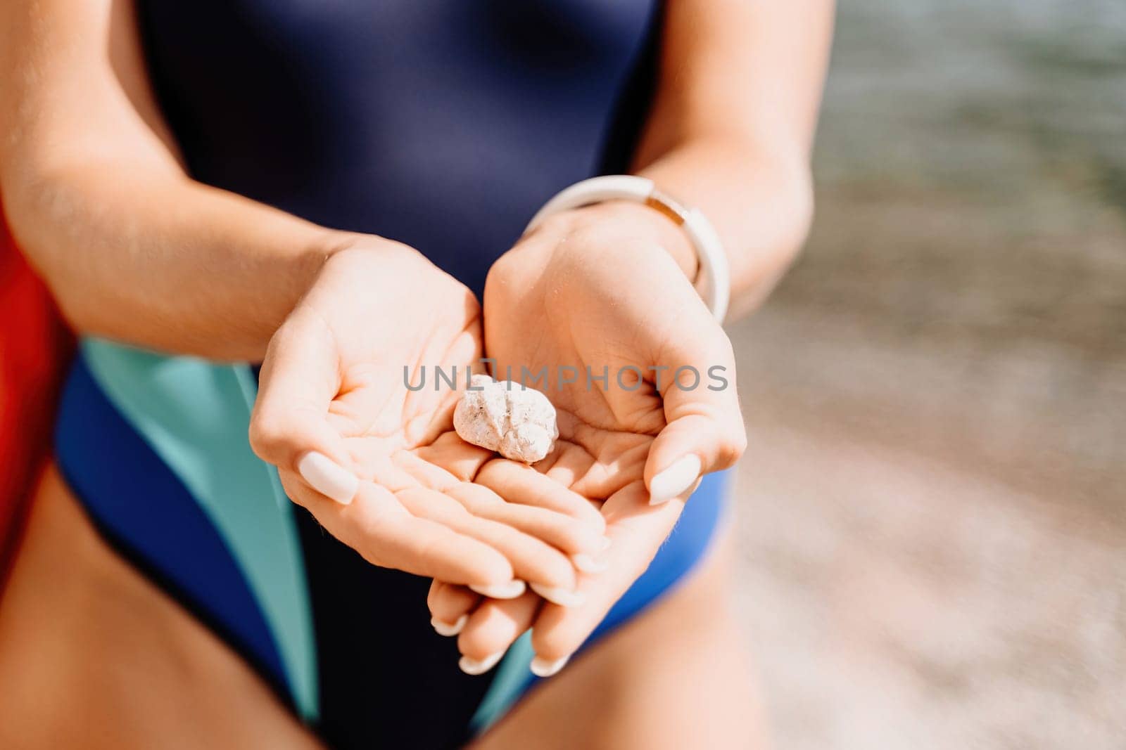 Beach vacation snapshot: A woman in a swimsuit holding a pebble in her hands, enjoying the serenity of the beach and the beauty of nature, creating a peaceful and relaxing atmosphere