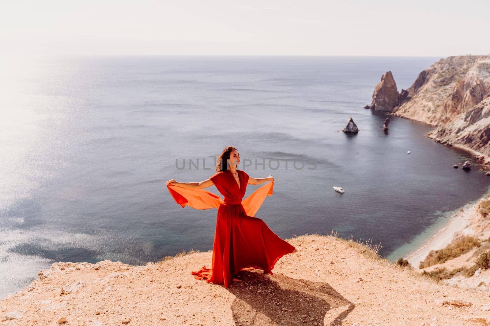 Woman red dress sea., posing on a rocky outcrop high above the sea. Girl on the nature on blue sky background. Fashion photo. by Matiunina