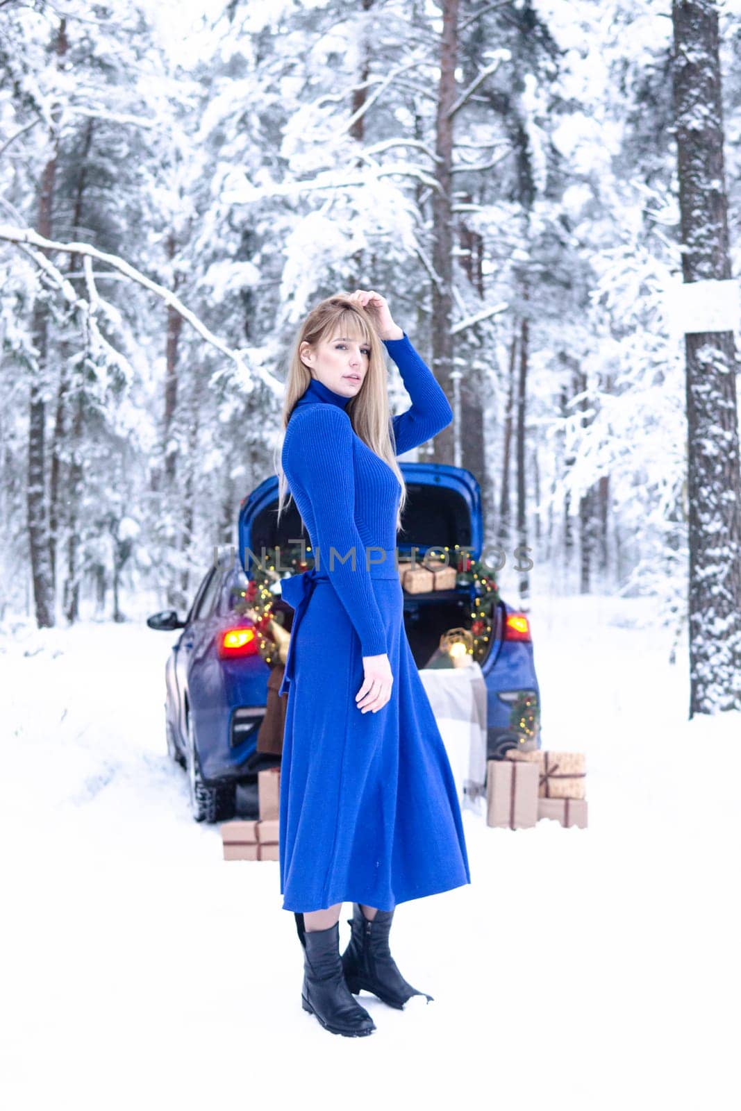 Woman in winter snowy forest in blue dress next to blue car decorated with Christmas decor. Christmas and winter holidays concept. by Annu1tochka