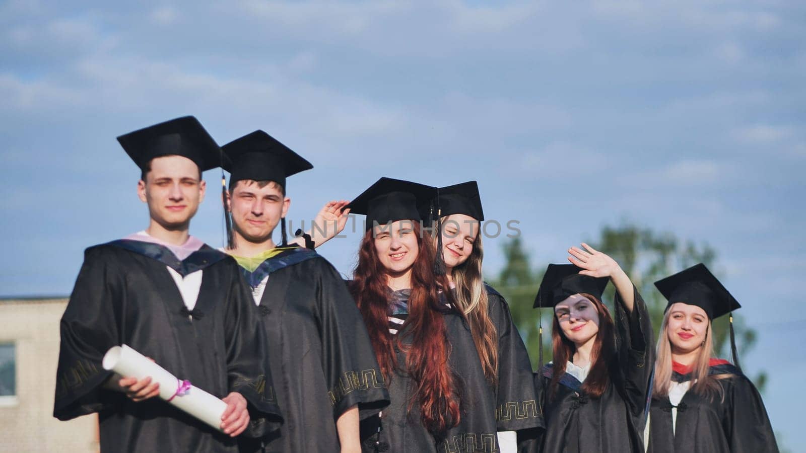 Cheerful graduates pose with raised diplomas on a sunny day. by DovidPro