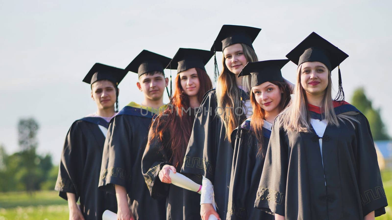 Cheerful graduates pose with raised diplomas on a sunny day