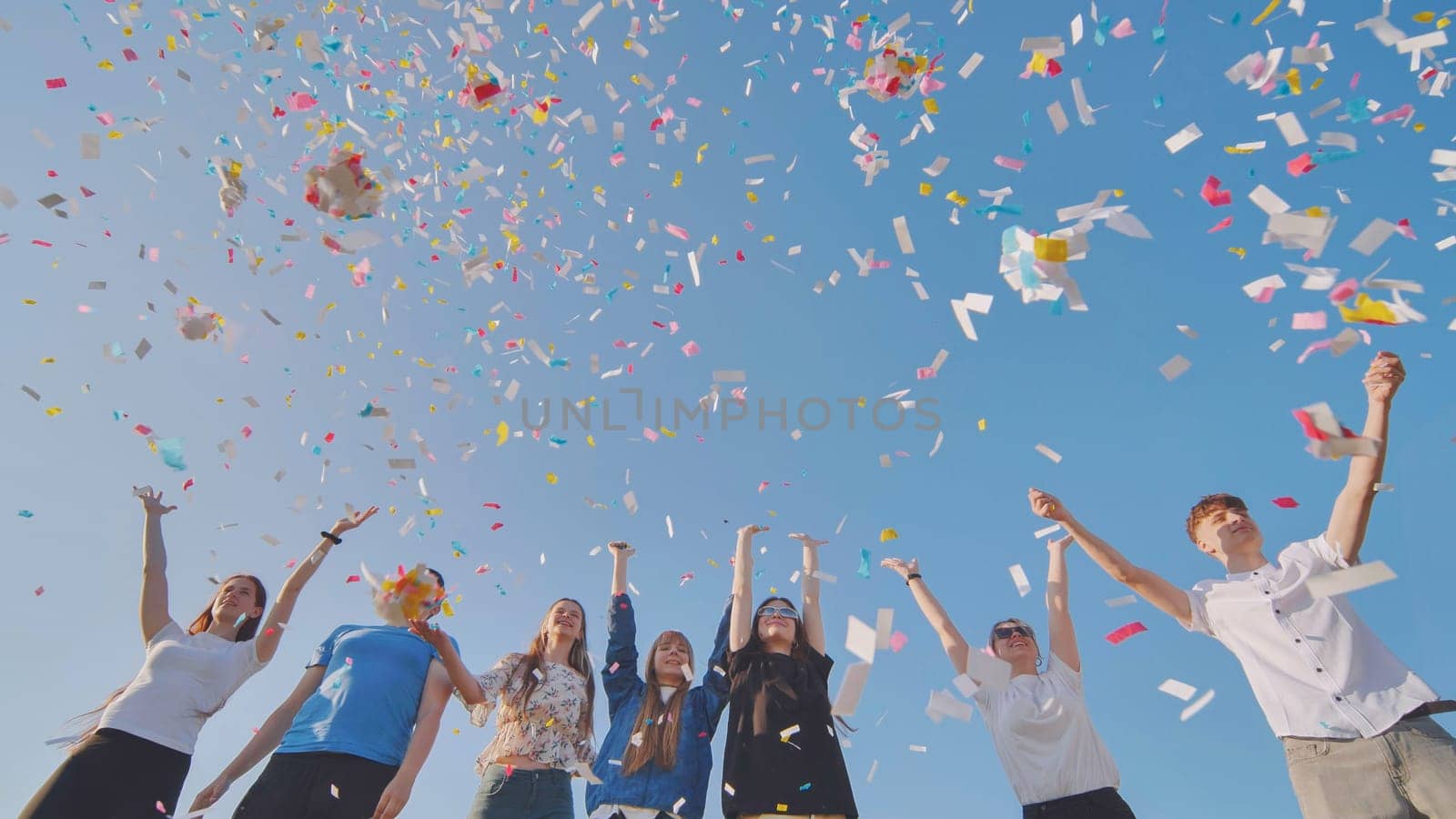 Friends toss colorful paper confetti from their hands. by DovidPro