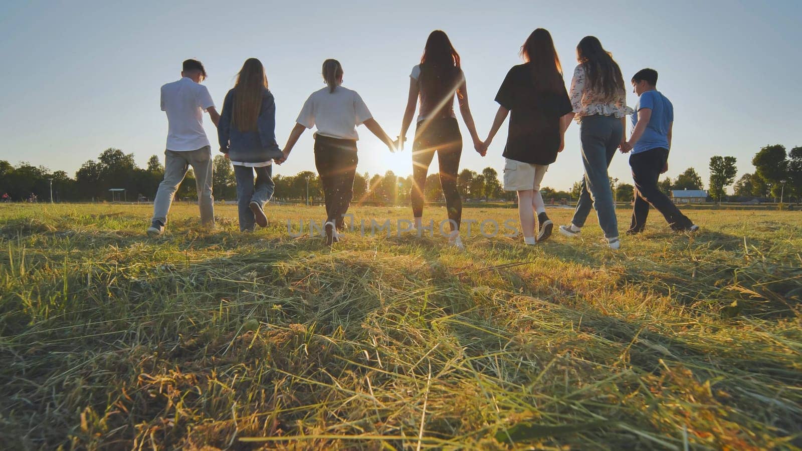 Friends at sunset holding hands walking towards the sun. by DovidPro