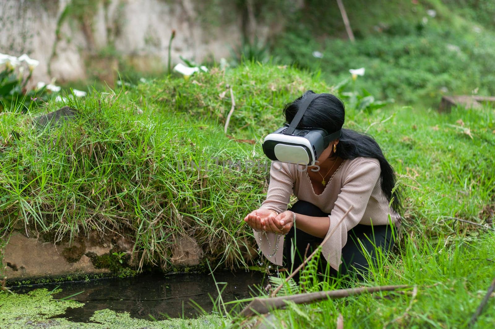a woman in the middle of nature with virtual reality goggles holding water from a river with both hands. water day by Raulmartin