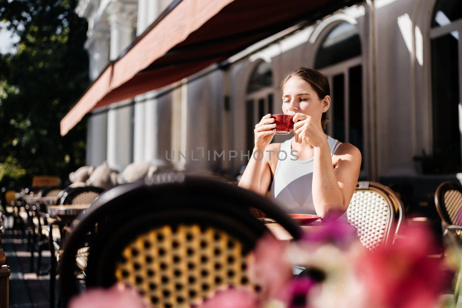 Portrait of happy woman sitting in a cafe outdoor drinking coffee. Woman while relaxing in cafe at table on street, dressed in a white T-shirt and jeans by Matiunina