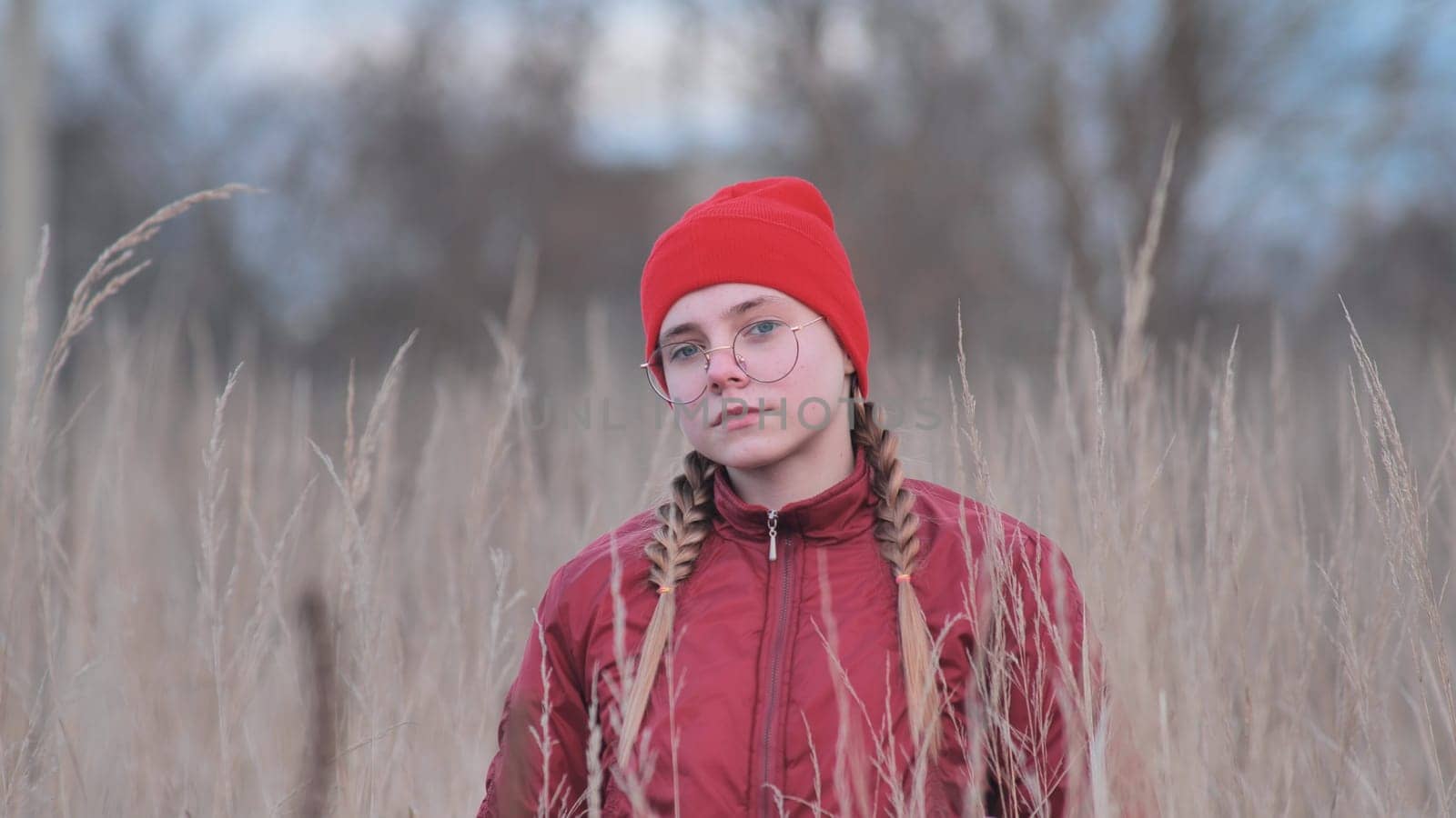 Portrait of a thoughtful teenage girl in glasses standing in tall grass in the fall