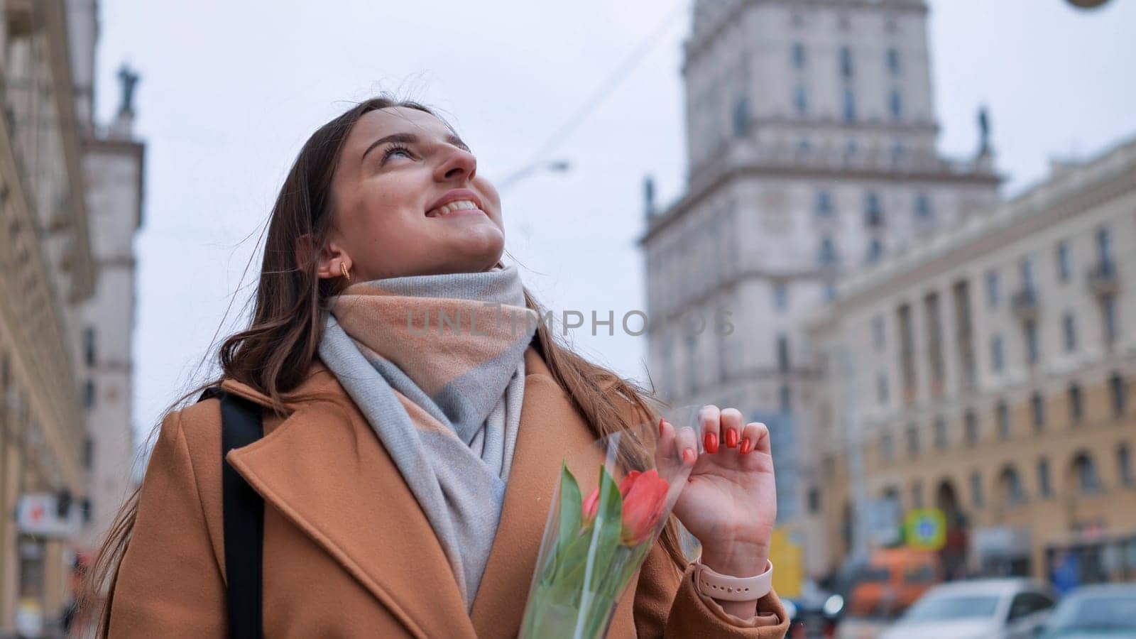 Portrait of a happy shade girl with a tulip in the background of the city in the cold season. by DovidPro