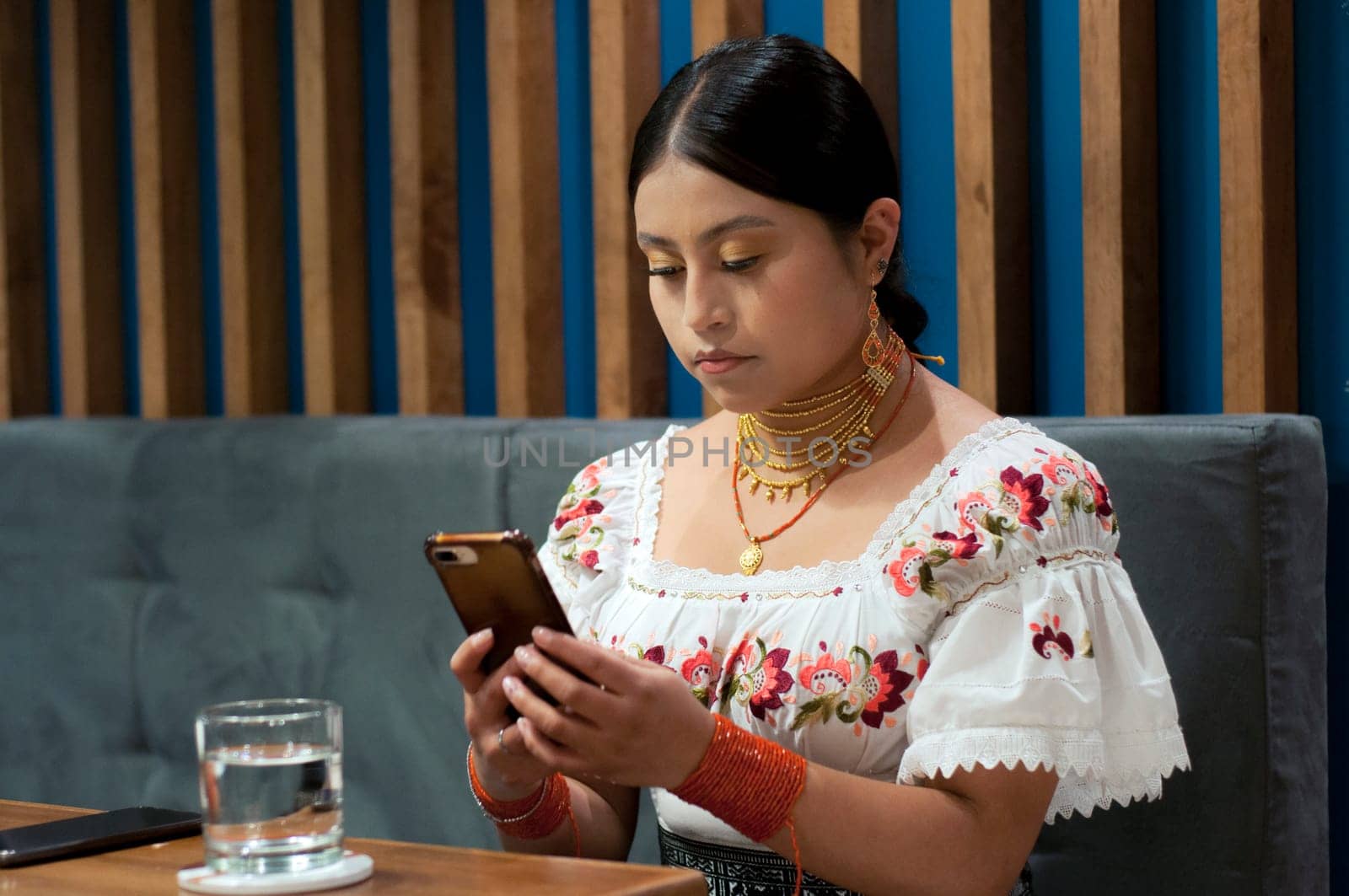 indigenous woman from otavalo, ecuador in traditional dress concentrating while writing a text message with her cell phone in a restaurant. High quality photo