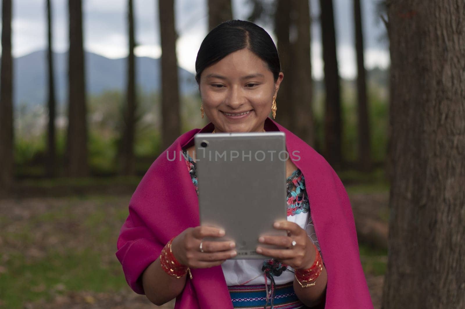 indigenous woman from the ecuadorian amazon very happy and excited sitting in a forest with a tablet talking online with her friends. by Raulmartin