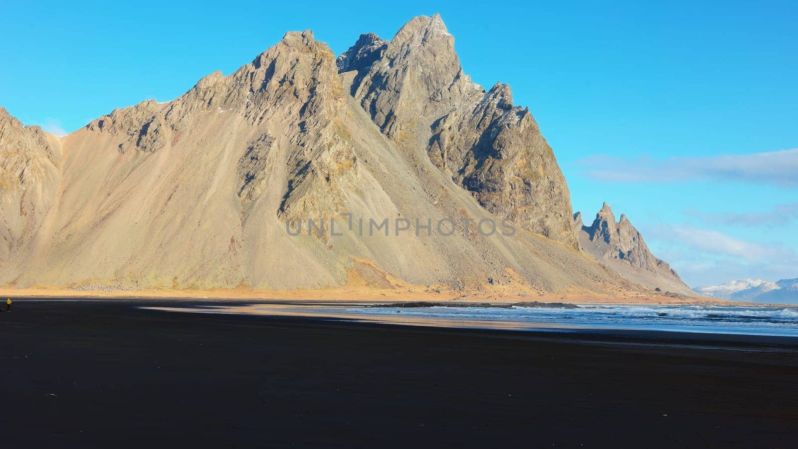 Vestrahorn mountains on arctic peninsula with natural black sand beach and beautiful skyline, sightseeing adventure. Ocean coastline shore and hills forming majestic landscape. Handheld shot.