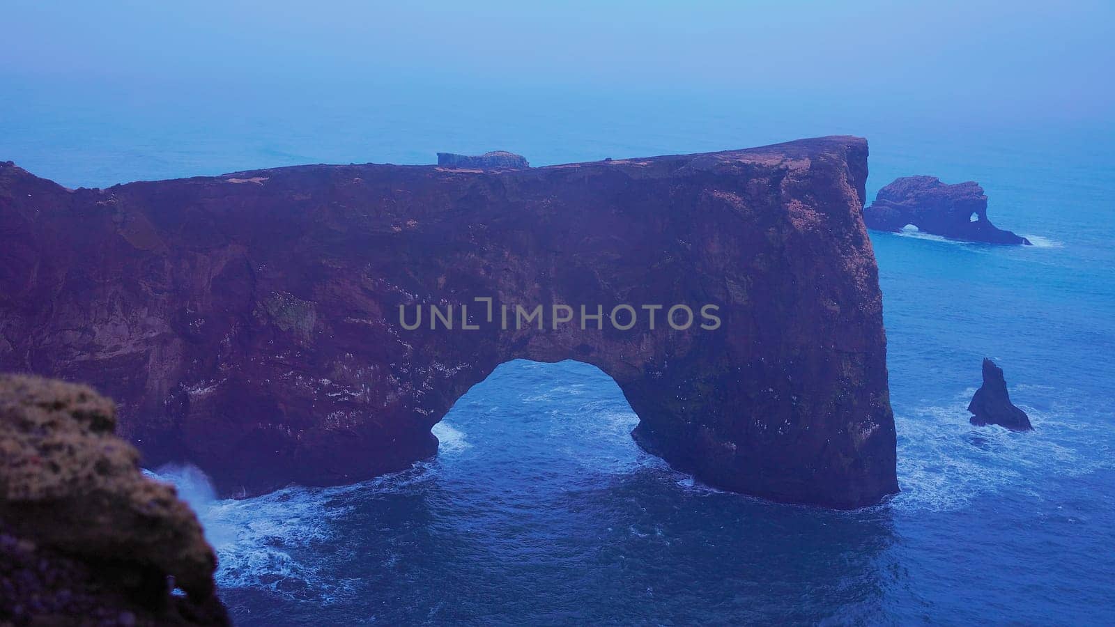 Stone coast arch on dyrholaey peninsula with natural foggy landscape and rock cliffs. Spectacular coastline gate in iceland, beautiful wild nature art with nordic design. Handheld shot.