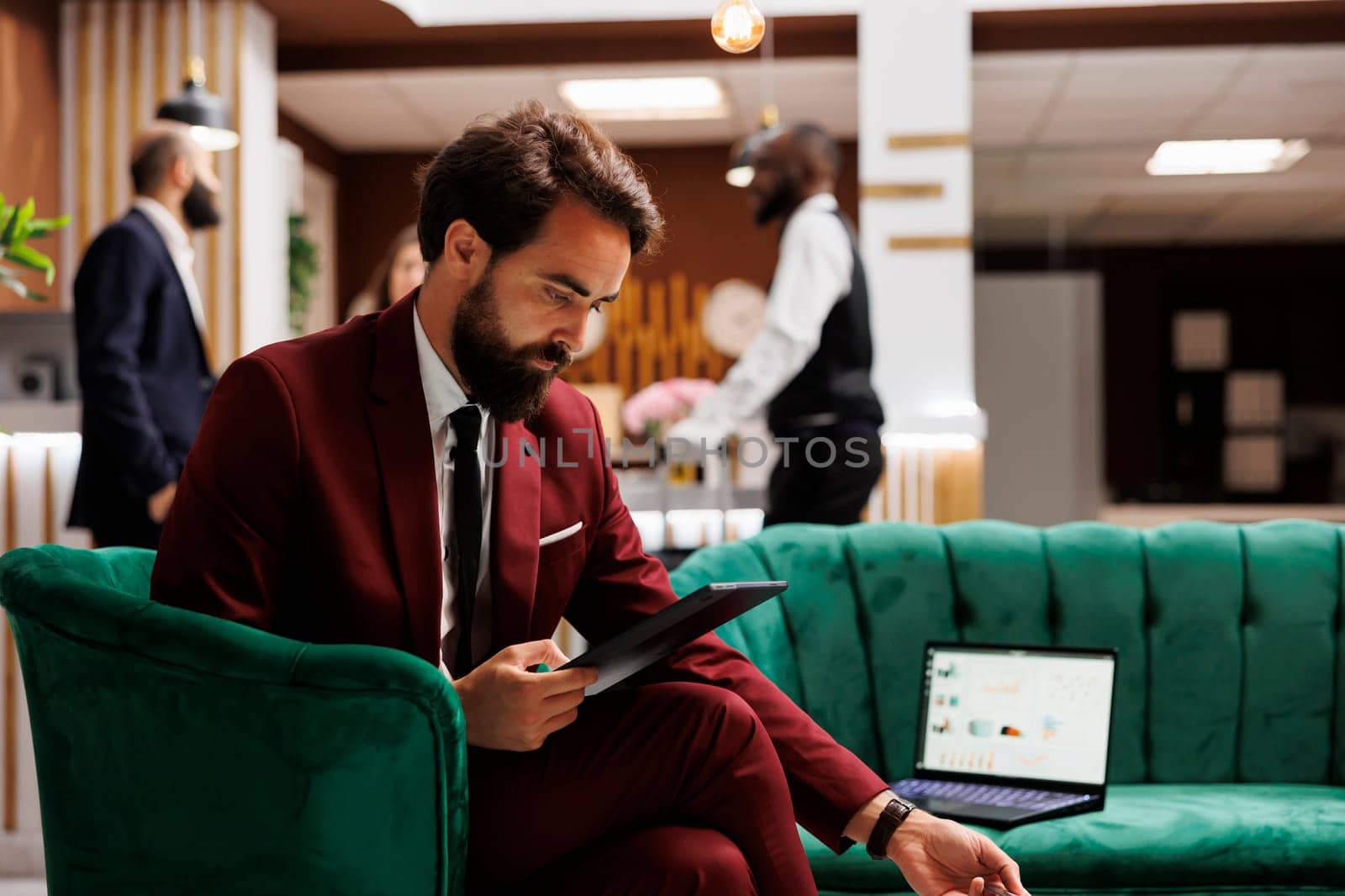 Businessman using tablet in hotel lobby, working on new ideas presentation for important upcoming meeting. Employee trying to create professional speech to impress executive board.