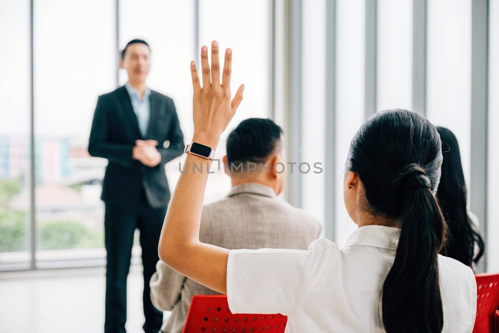 A diverse crowd in a corporate event raises their hands for questions, voting, or volunteering, emphasizing teamwork and audience interaction during the conference by Sorapop