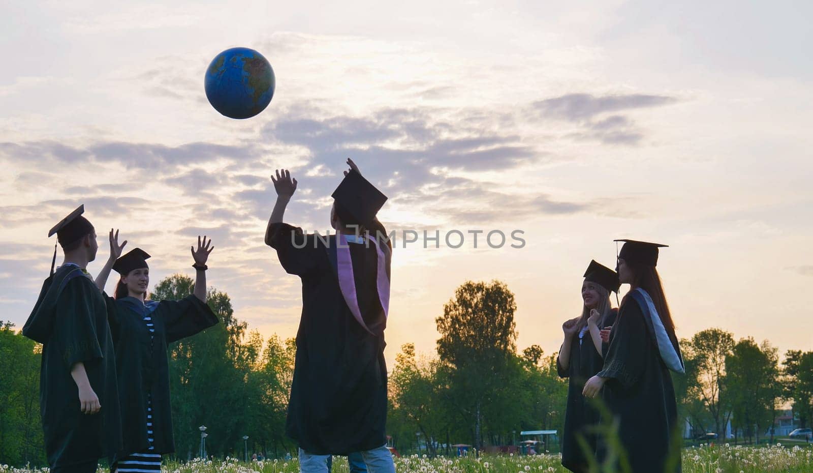 Graduates in costume playing with a ball at sunset