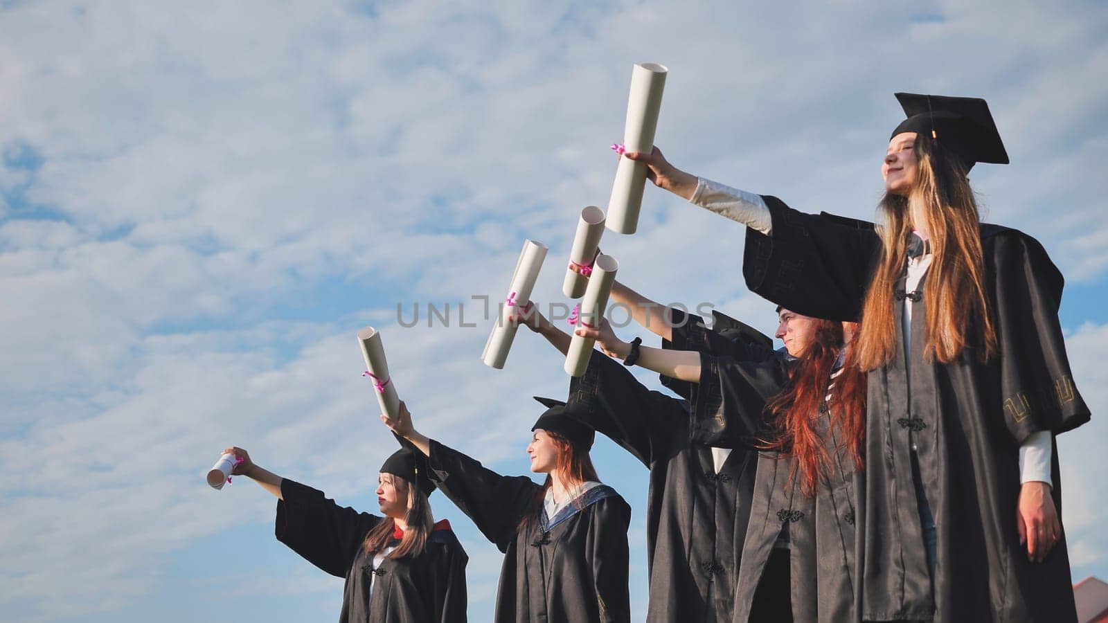 Cheerful graduates pose with raised diplomas on a sunny day