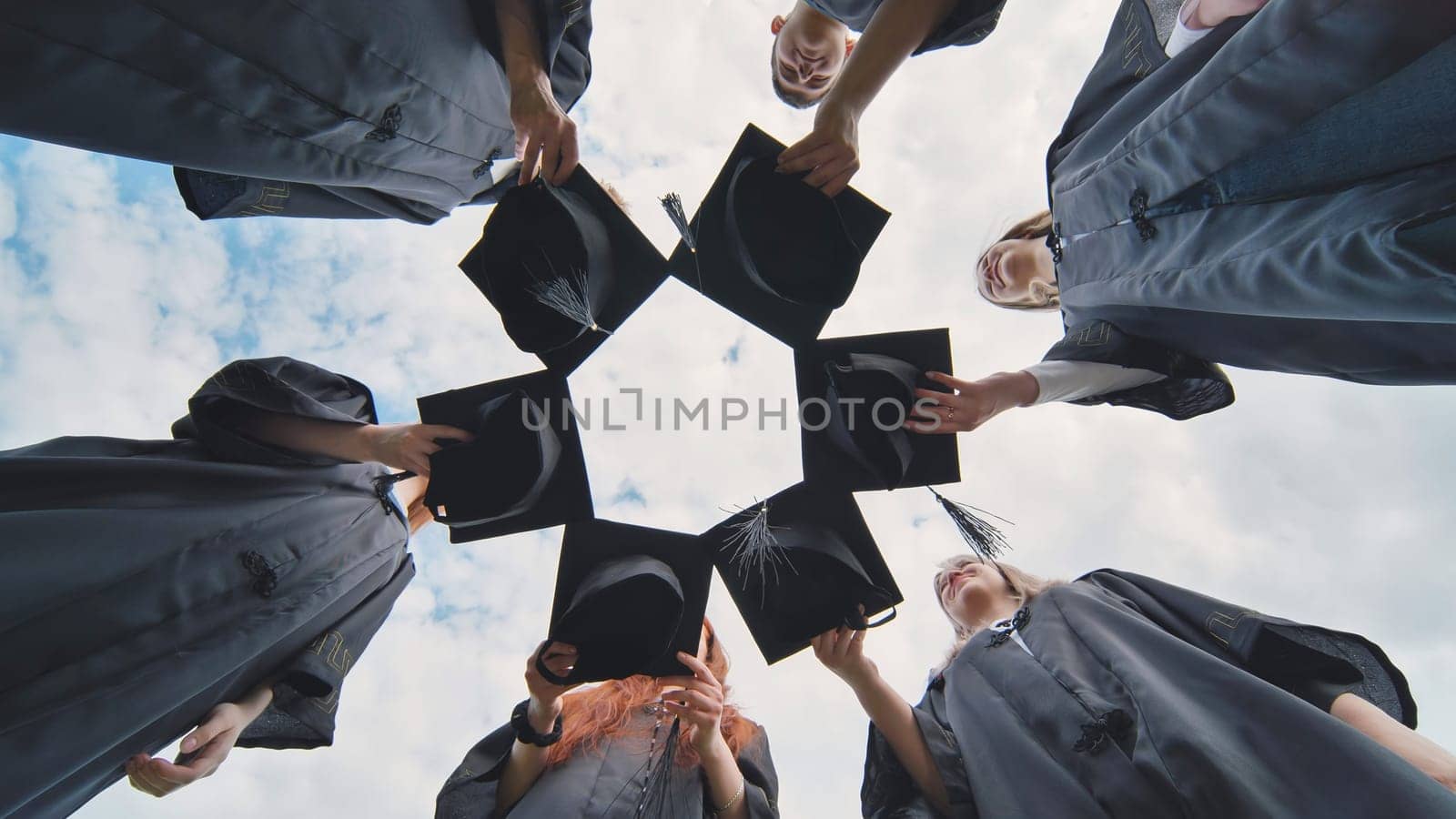 Graduates in black robes join their caps in a circle