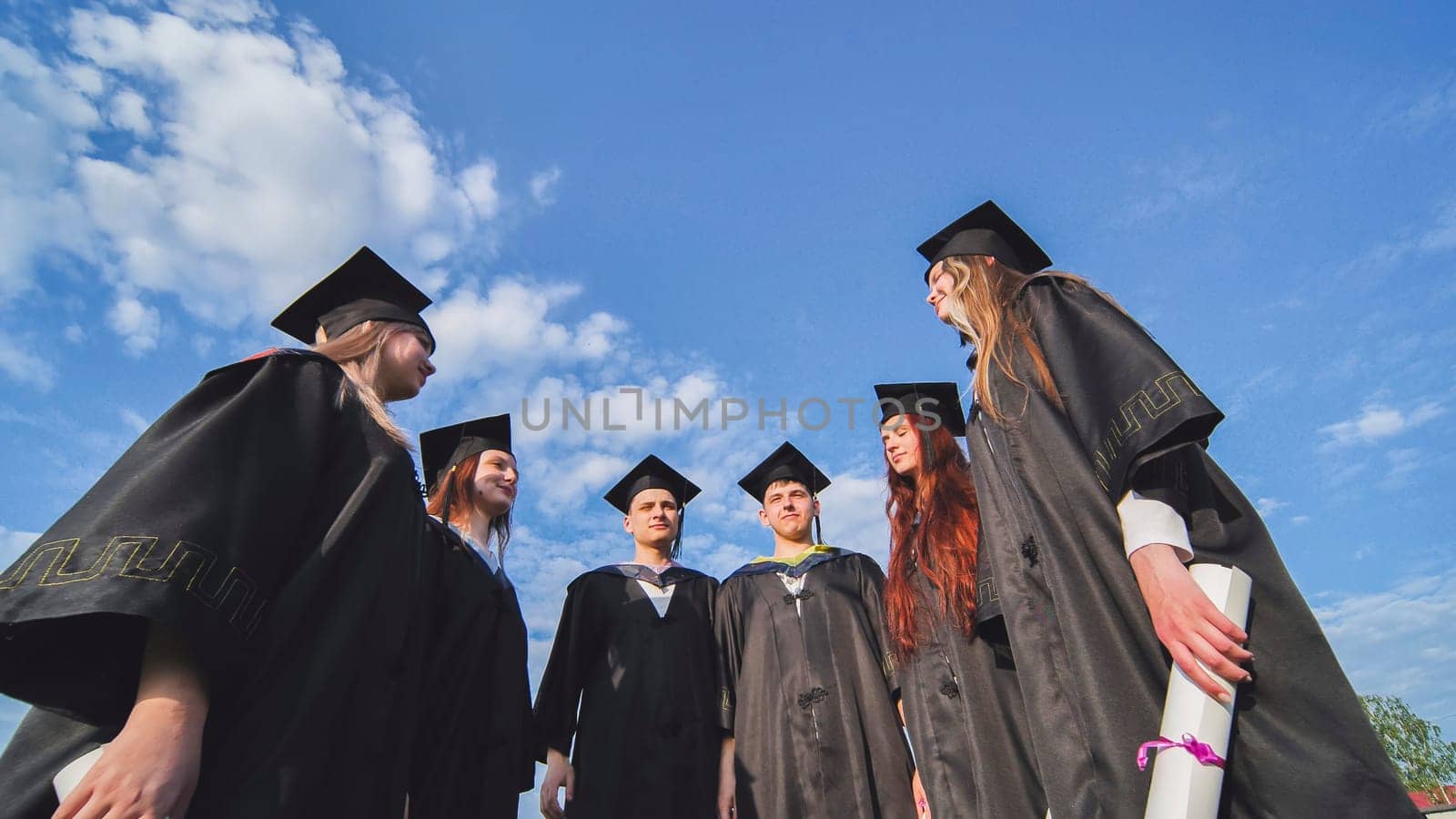 Graduating students stand in a semicircle on a sunny summer afternoon