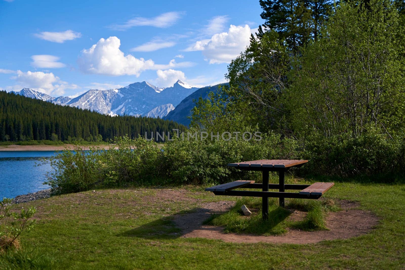 A picnic table on the edge of a lake overlooking the Canadian mountains in Alberta. by Try_my_best