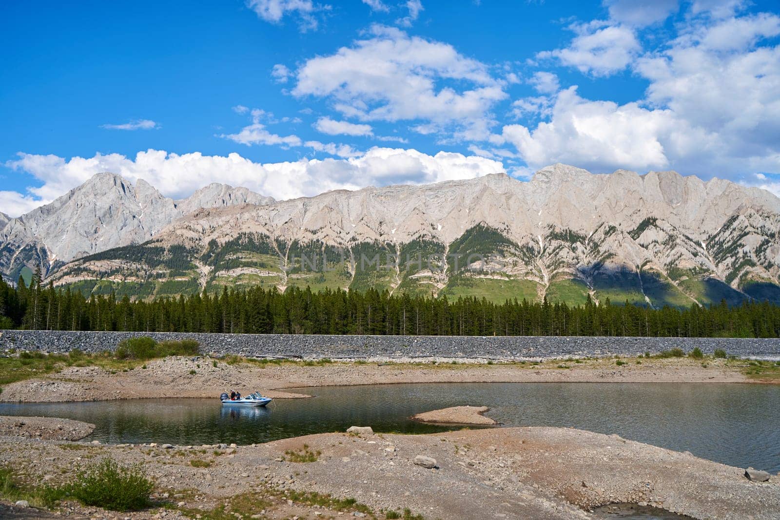 A fishing boat with fishermen fishing on a beautiful natural mountain lake on a sunny summer day with rocky mountains in the province of Alberta, Canada. by Try_my_best