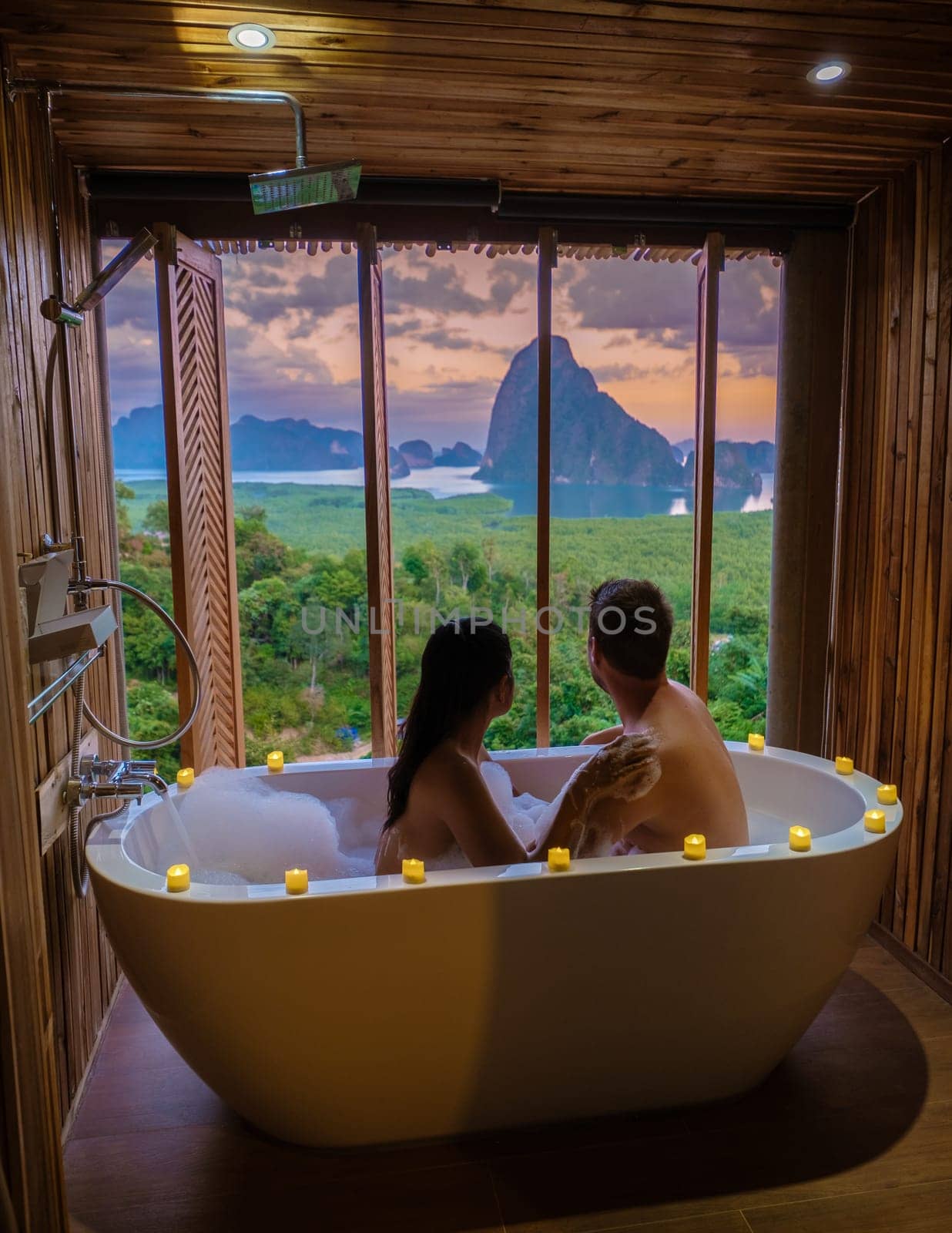 A couple of men and a woman in a bathtub looking at the sunset over Sametnangshe viewpoint mountains in Phangnga Bay with mangrove forest in the Andaman Sea in Phangnga, Thailand