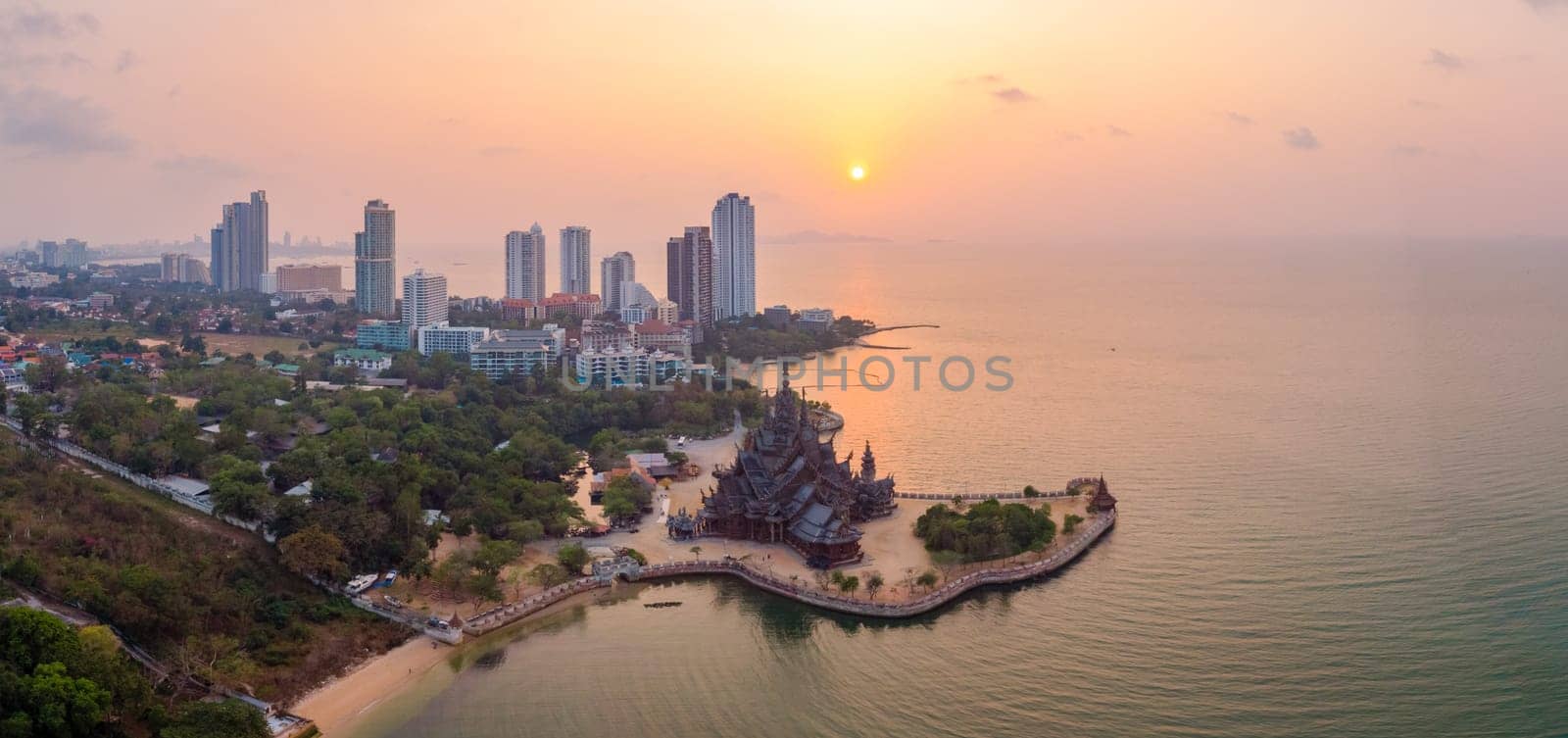 The Sanctuary of Truth wooden temple in Pattaya Thailand at sunset seen from the beach by the ocean, drone aerial view at Pattaya skyline