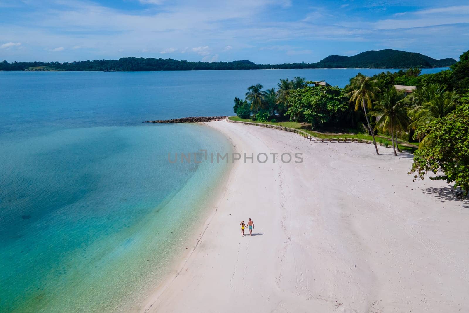 couple walking at the beach of Koh Kham Trat Thailand, aerial view of the tropical island near Koh Mak Thailand. white sandy beach with palm trees and big black boulder stones in the ocean