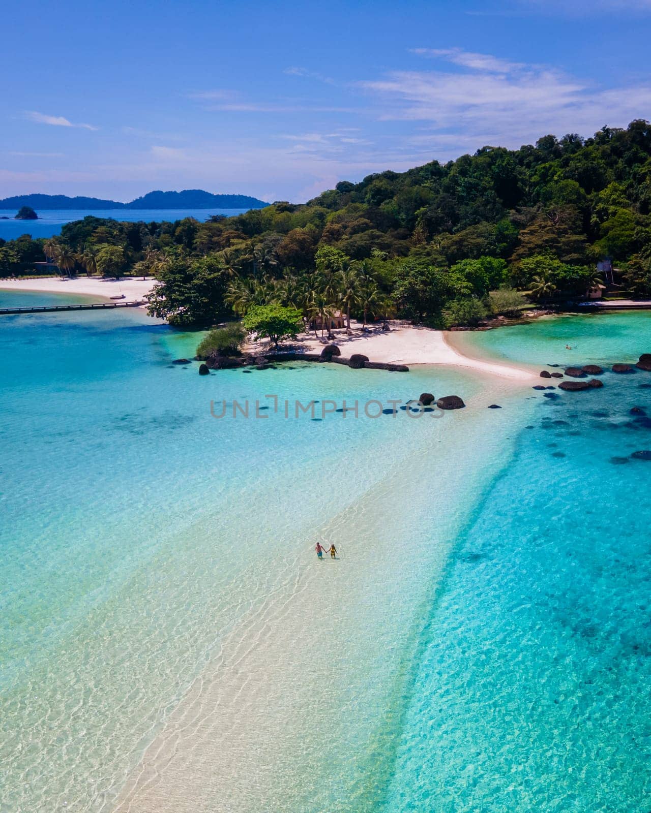 couple walking at the beach of Koh Kham Trat Thailand tropical island near Koh Mak Thailand. white sandy beach with palm trees and big black boulder stones in the ocean