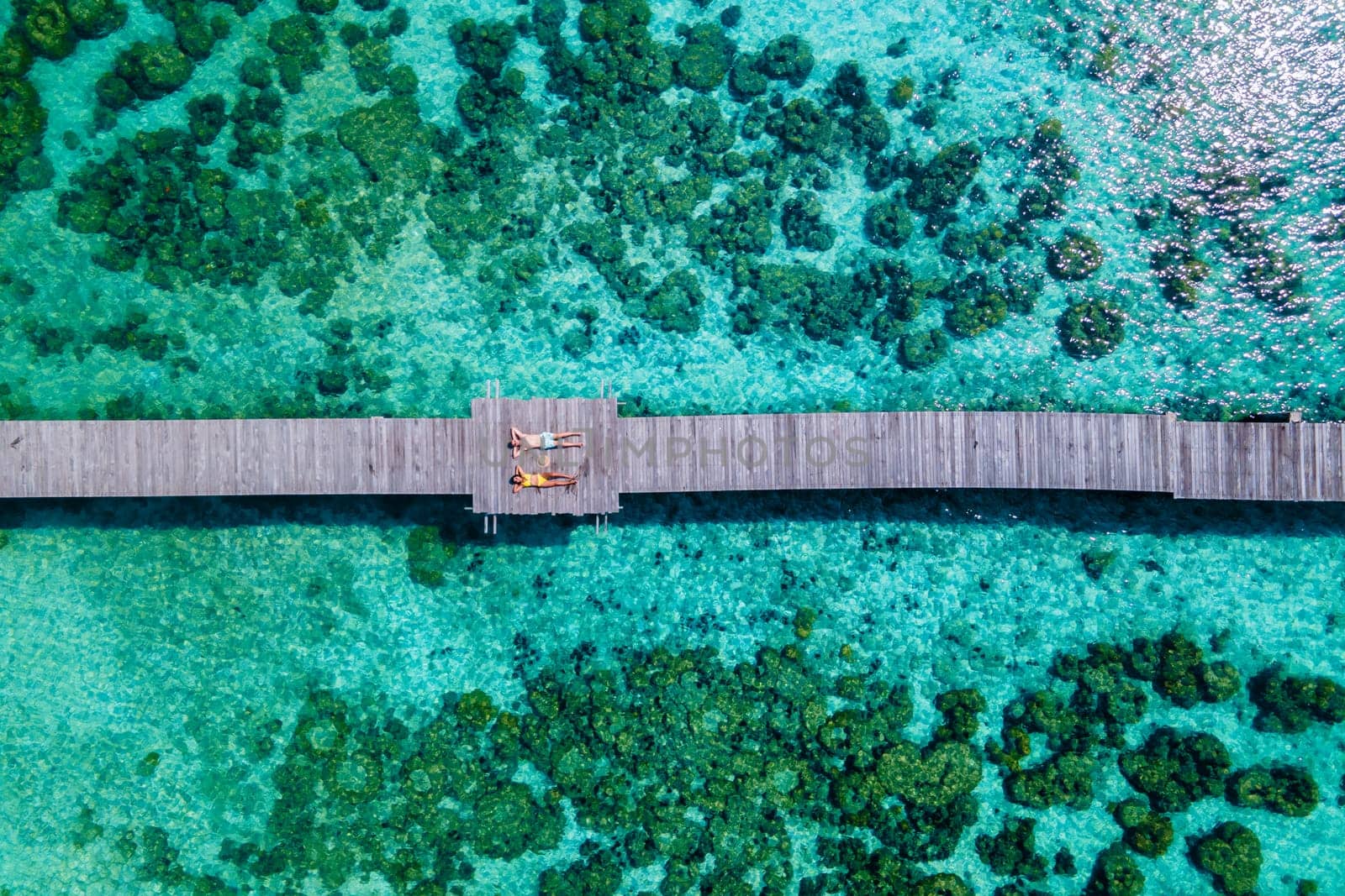 couple of men and woman lying down on a wooden pier in the oceanof Koh Kham Trat Thailand by fokkebok