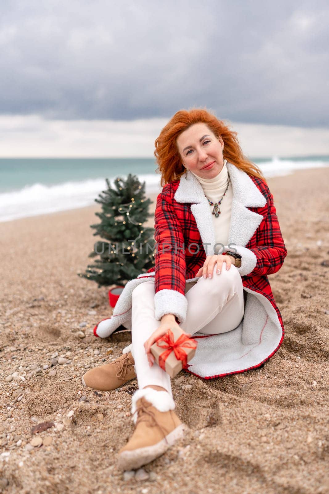Lady in plaid shirt holding a gift in his hands enjoys beach with Christmas tree. Coastal area. Christmas, New Year holidays concep by Matiunina