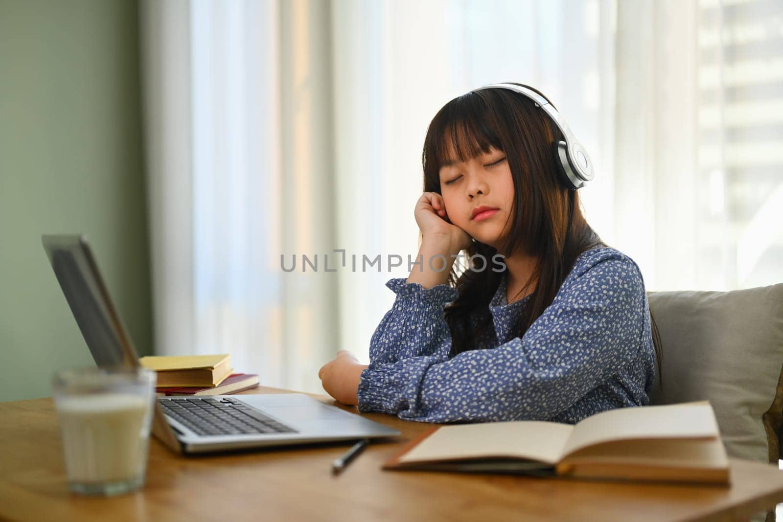 Tired elementary student girl sleeping while doing her homework at work desk