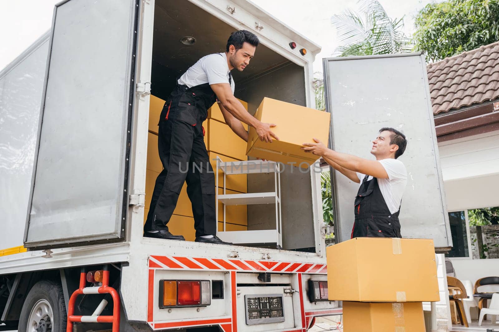 Workers in uniform exhibit teamwork unloading cardboard boxes from the moving truck for customer relocation. The company efficient service ensures a happy move. Moving Day by Sorapop