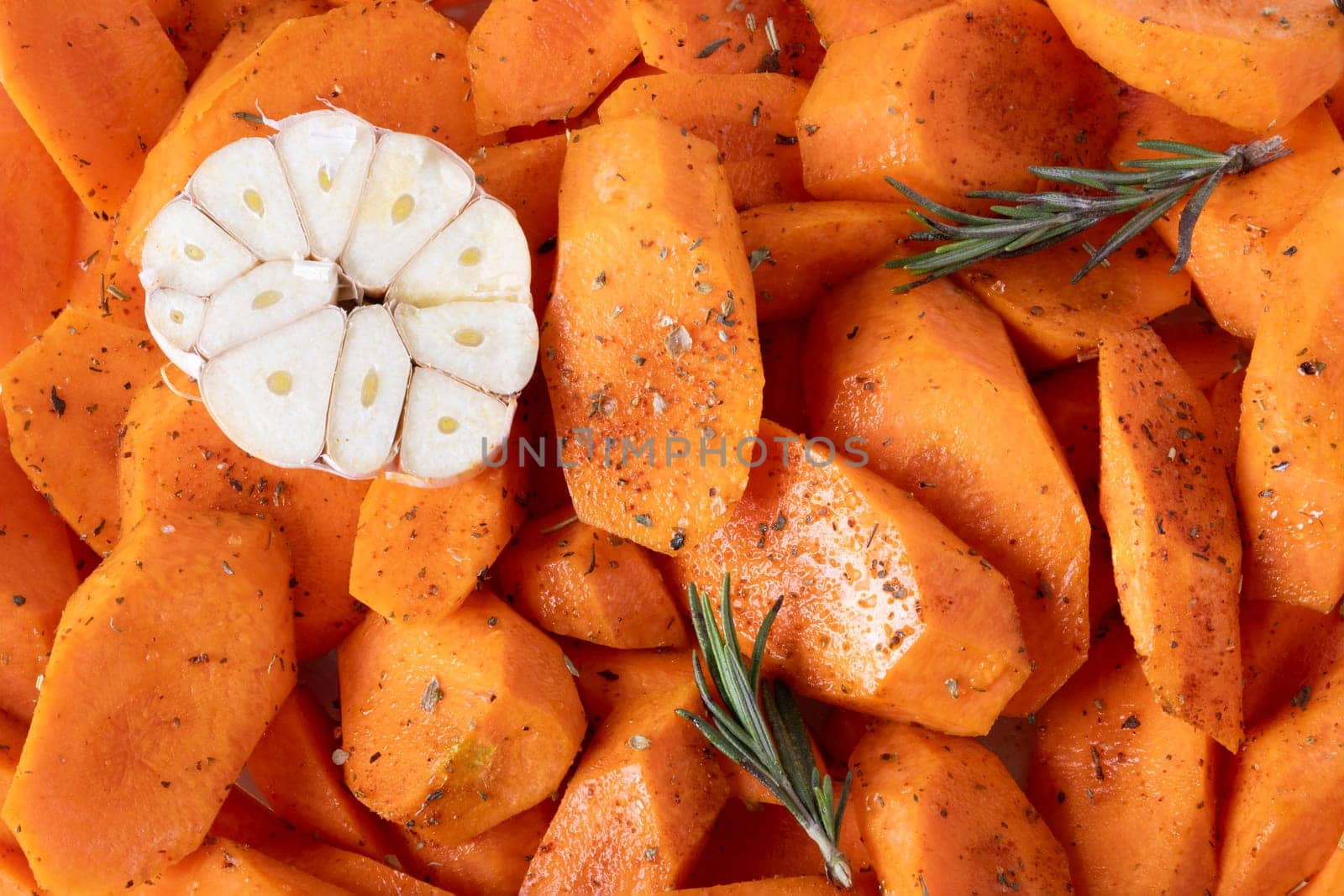 Fresh carrots cut into pieces, seasoned with spices and olive oil, lie on baking tray. Food background. Selective focus.