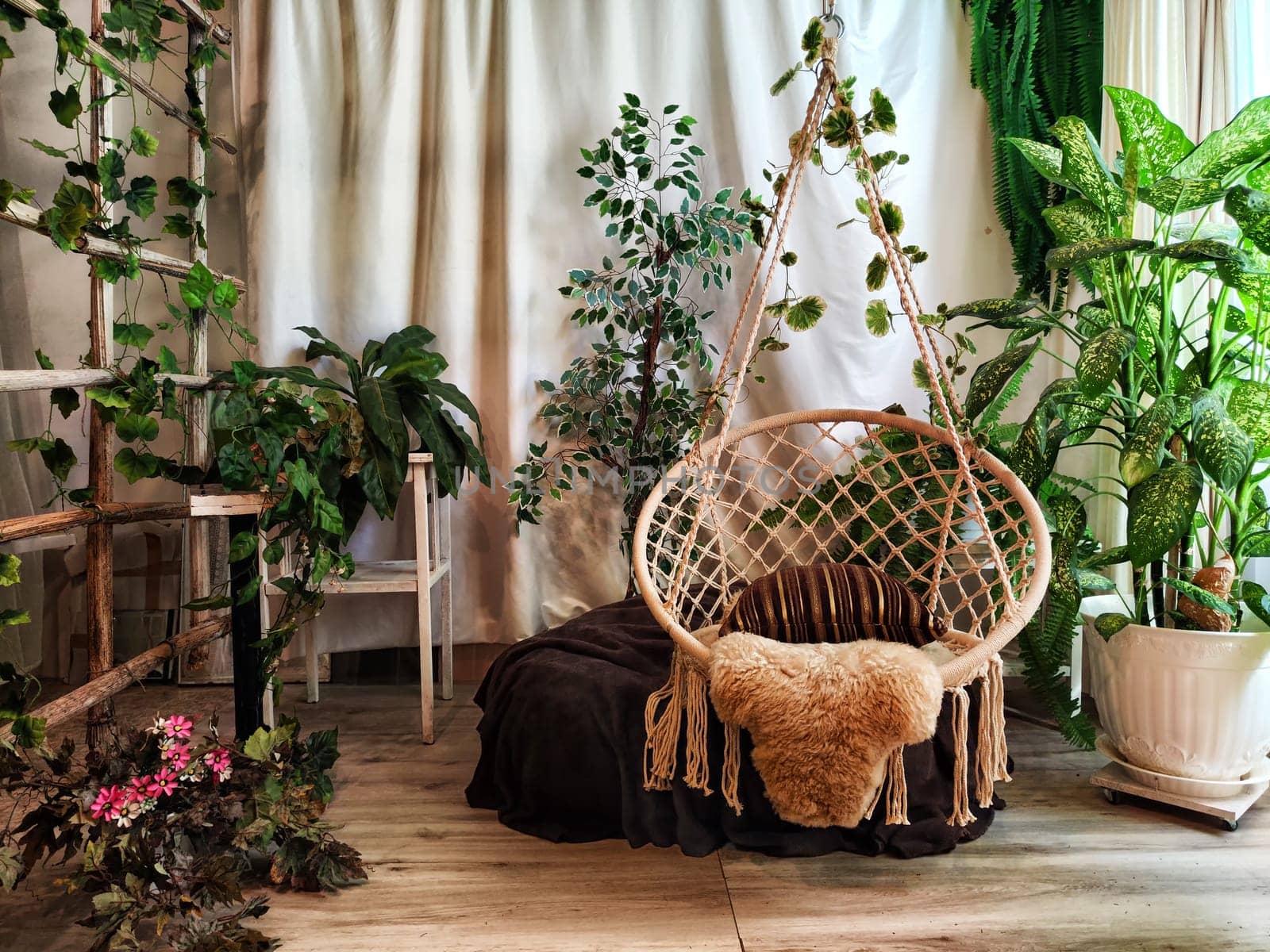 Modern cozy beautiful room with a braided rope macrame chair, green plants and a window with curtains. Interior and background. Location for photo shooting