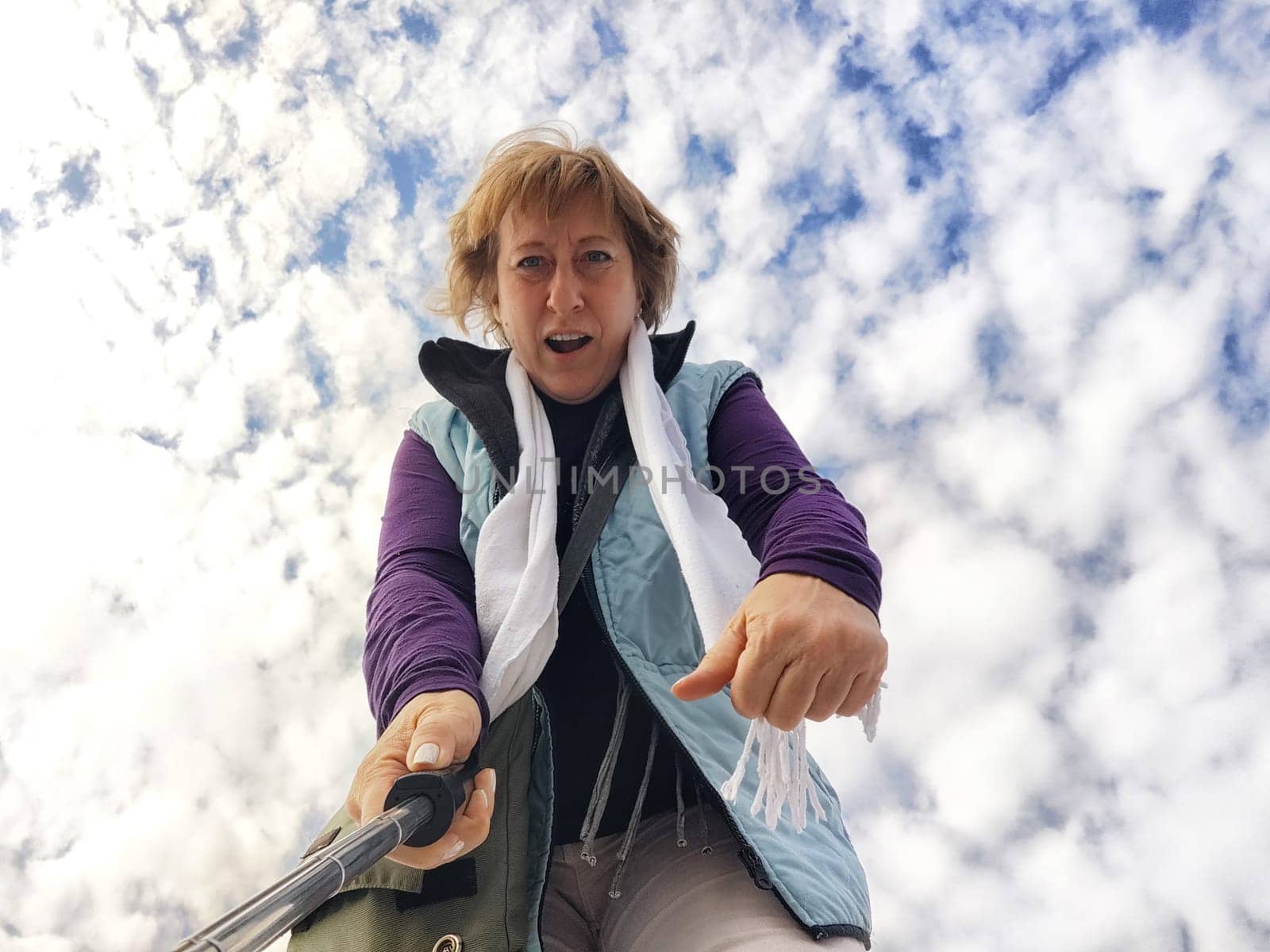 A happy, funny, funny adult girl takes a selfie against a blue sky with white clouds. A middle-aged woman poses on the phone in nature in autumn or spring by keleny