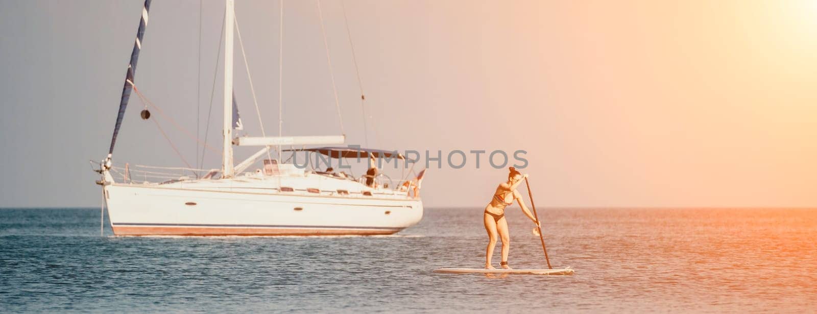 Sea woman sup. Silhouette of happy middle aged tanned woman in rainbow bikini, surfing on SUP board, confident paddling through water surface. Idyllic sunset. Active lifestyle at sea or river. by panophotograph