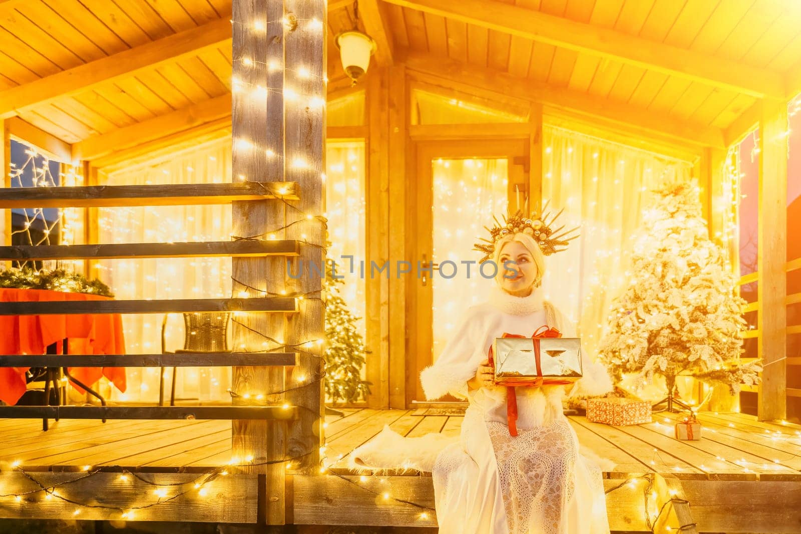 A woman in a white dress holding a gift box in front of a Christmas tree. by panophotograph