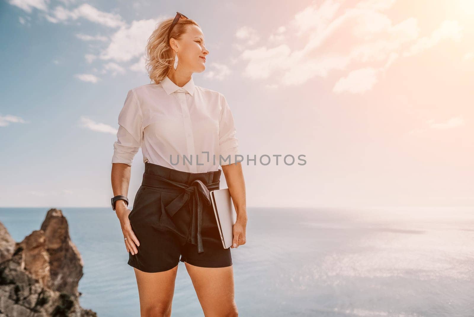 Digital nomad, Business woman working on laptop by the sea. Pretty lady typing on computer by the sea at sunset, makes a business transaction online from a distance. Freelance, remote work on vacation