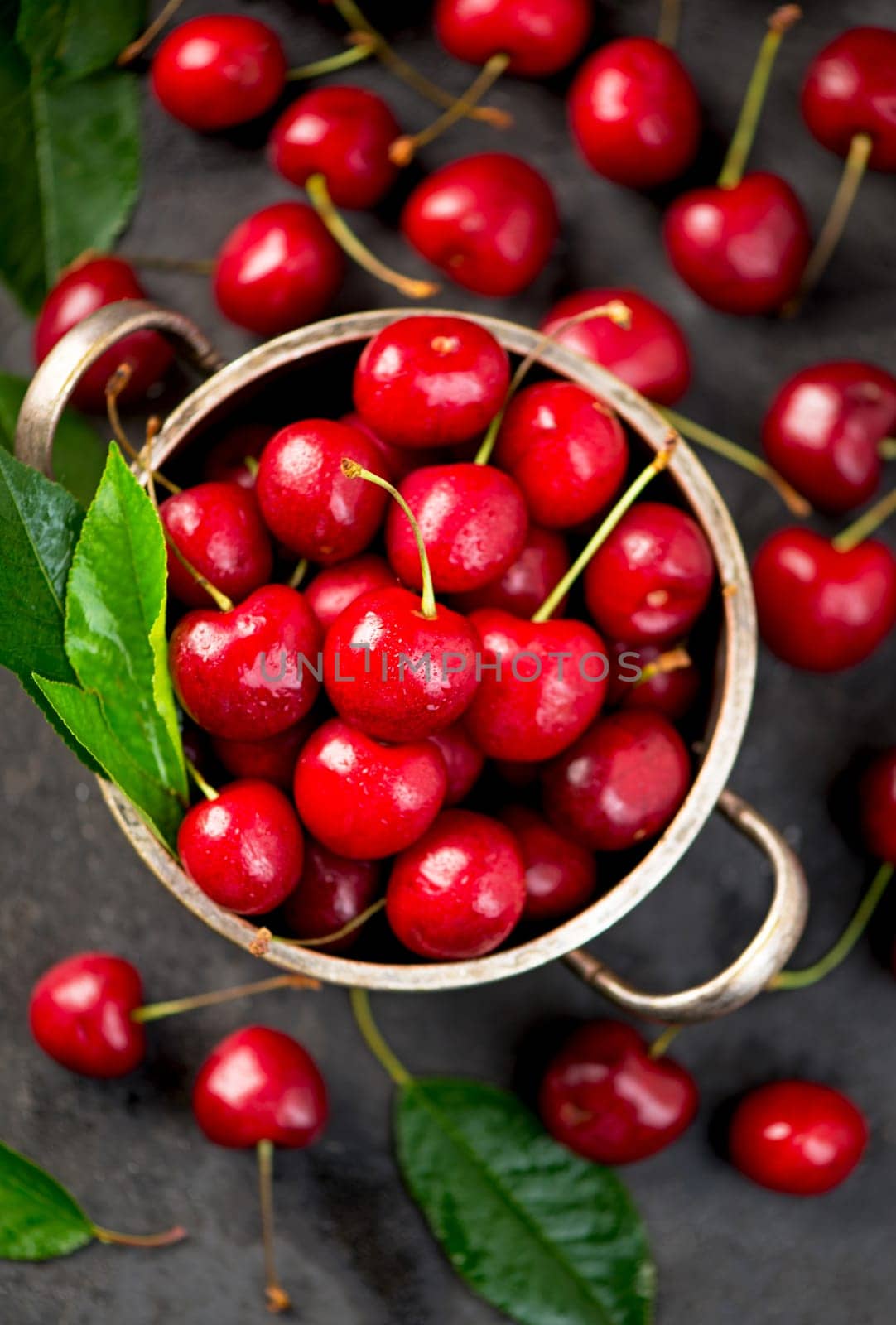 Ripe sweet cherry berry with leaves in a pan on a black wooden board by aprilphoto