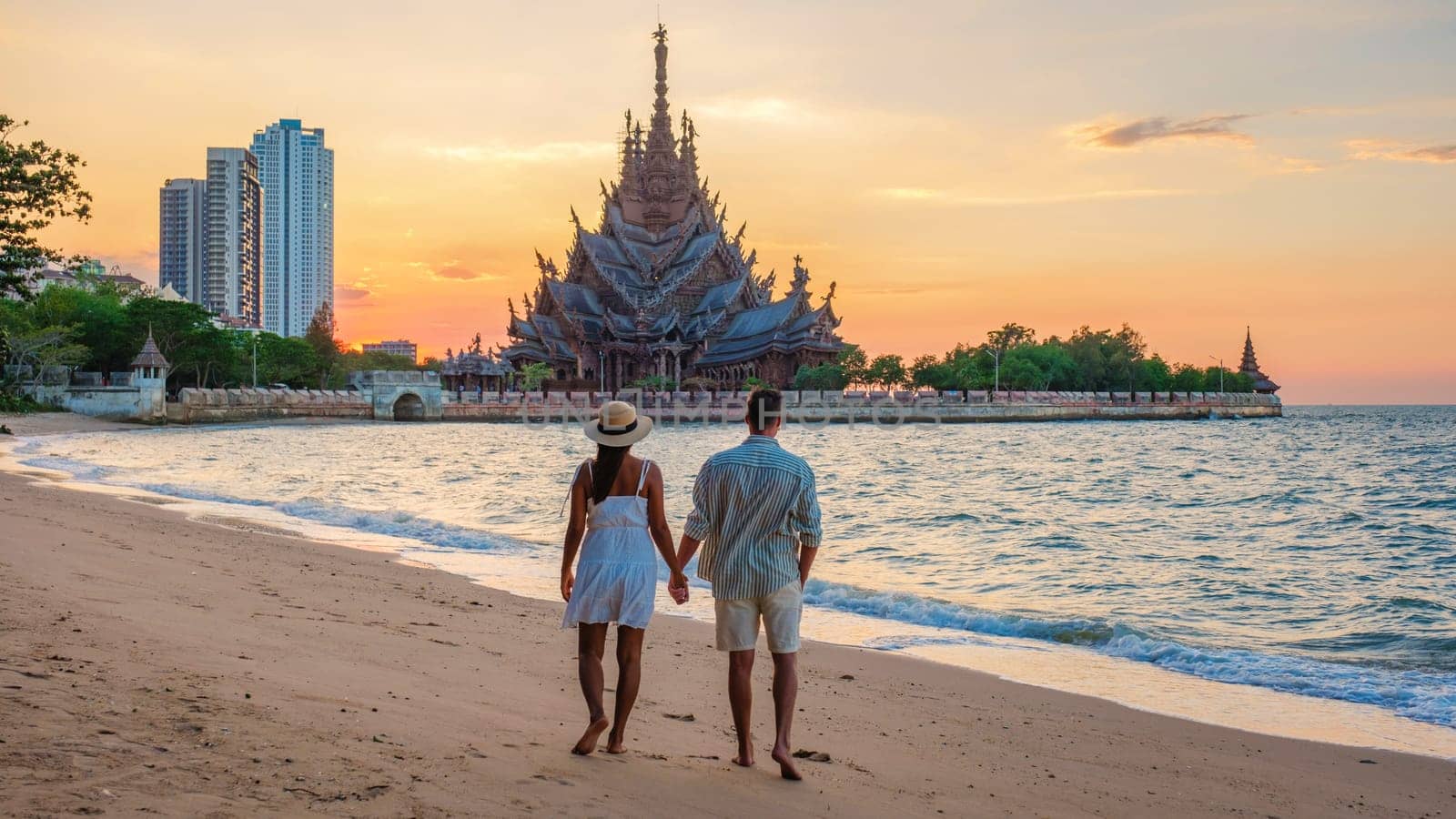 A diverse multiethnic couple of men and women visit The Sanctuary of Truth wooden temple in Pattaya Thailand