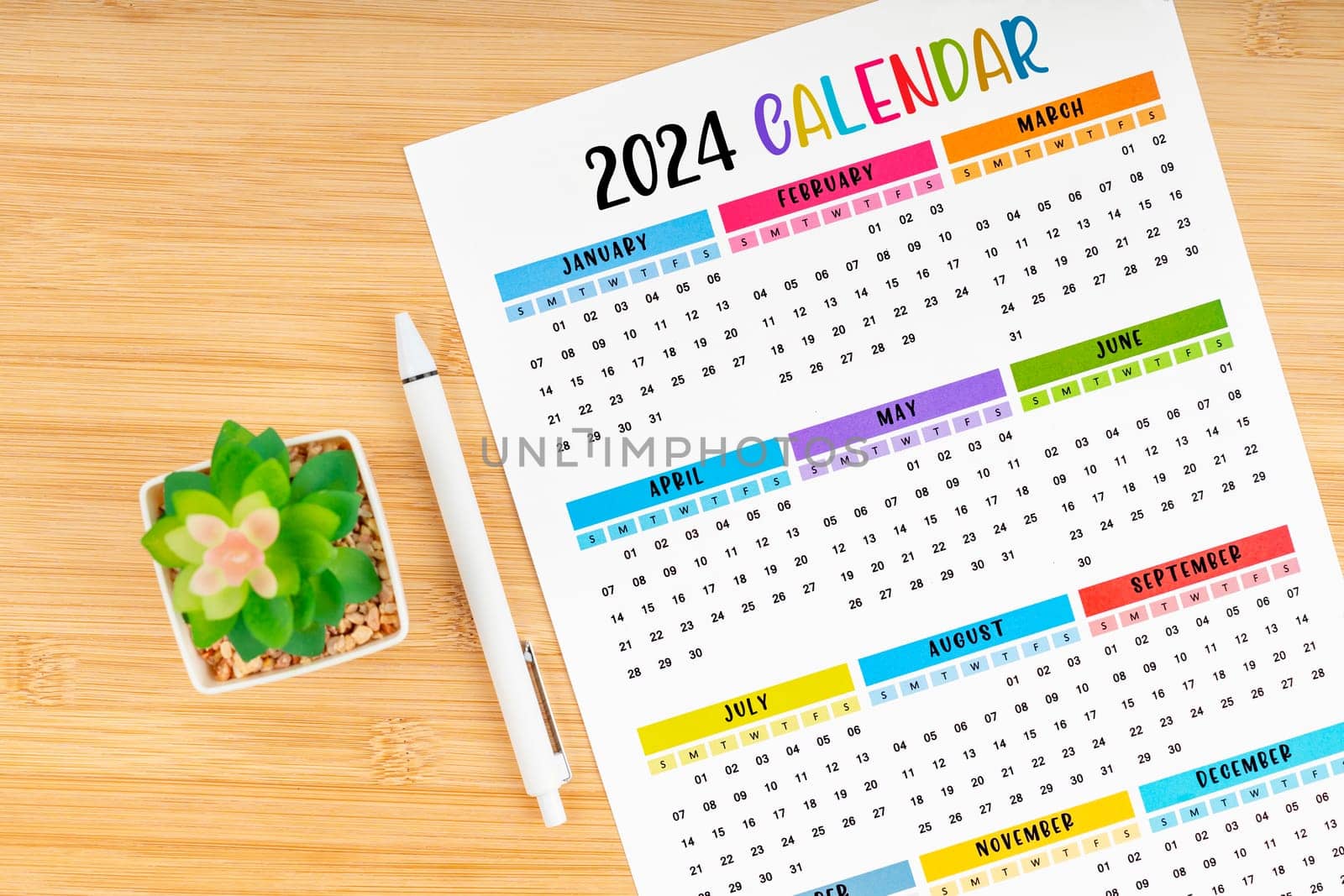 12 months desk calendar 2024 and pen with flower pot on wooden background.