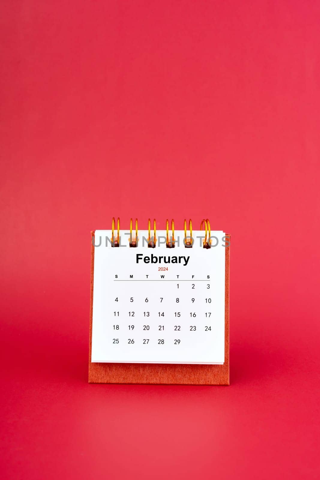 February 2024 white mini desk calendar on red color background.
